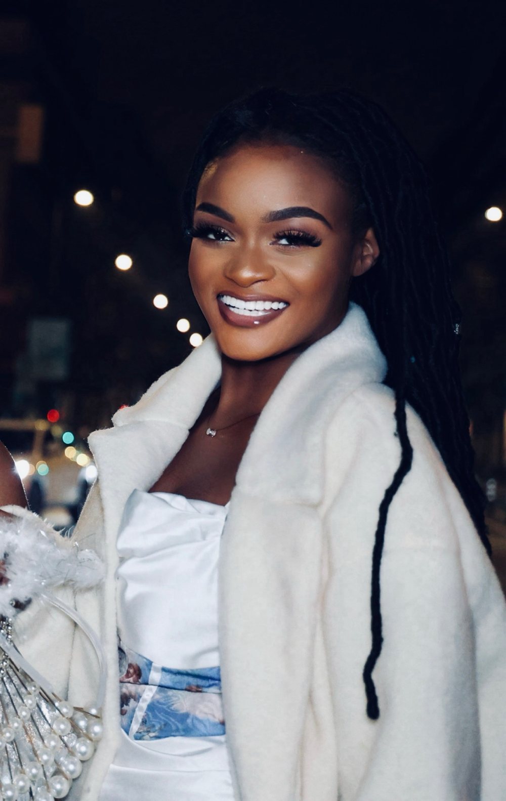 Divine-Gloria BATEKOUAHOU, souriante, de nuit dans une rue éclairée